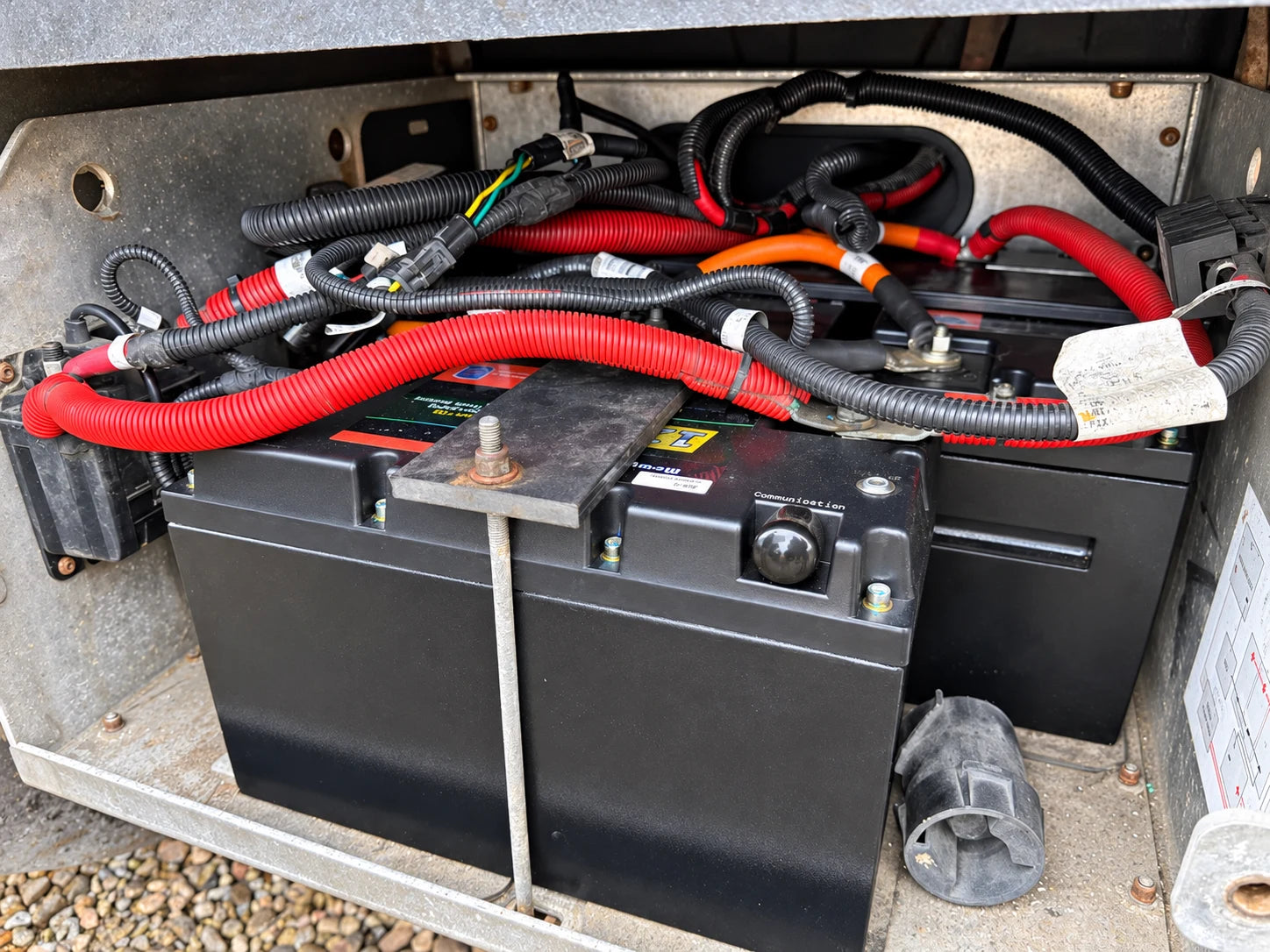 Dual-purpose battery installation with red cable looms and a retaining strap