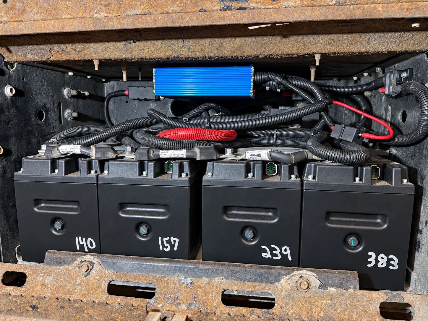 Four batteries installed below a blue electrical module in a truck compartment