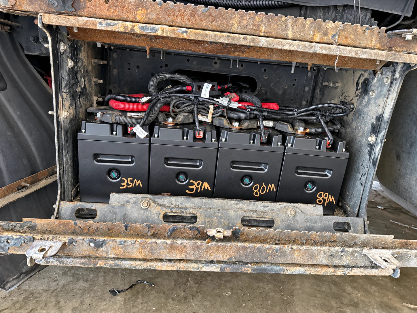 Four batteries with orange service markings mounted in a truck compartment