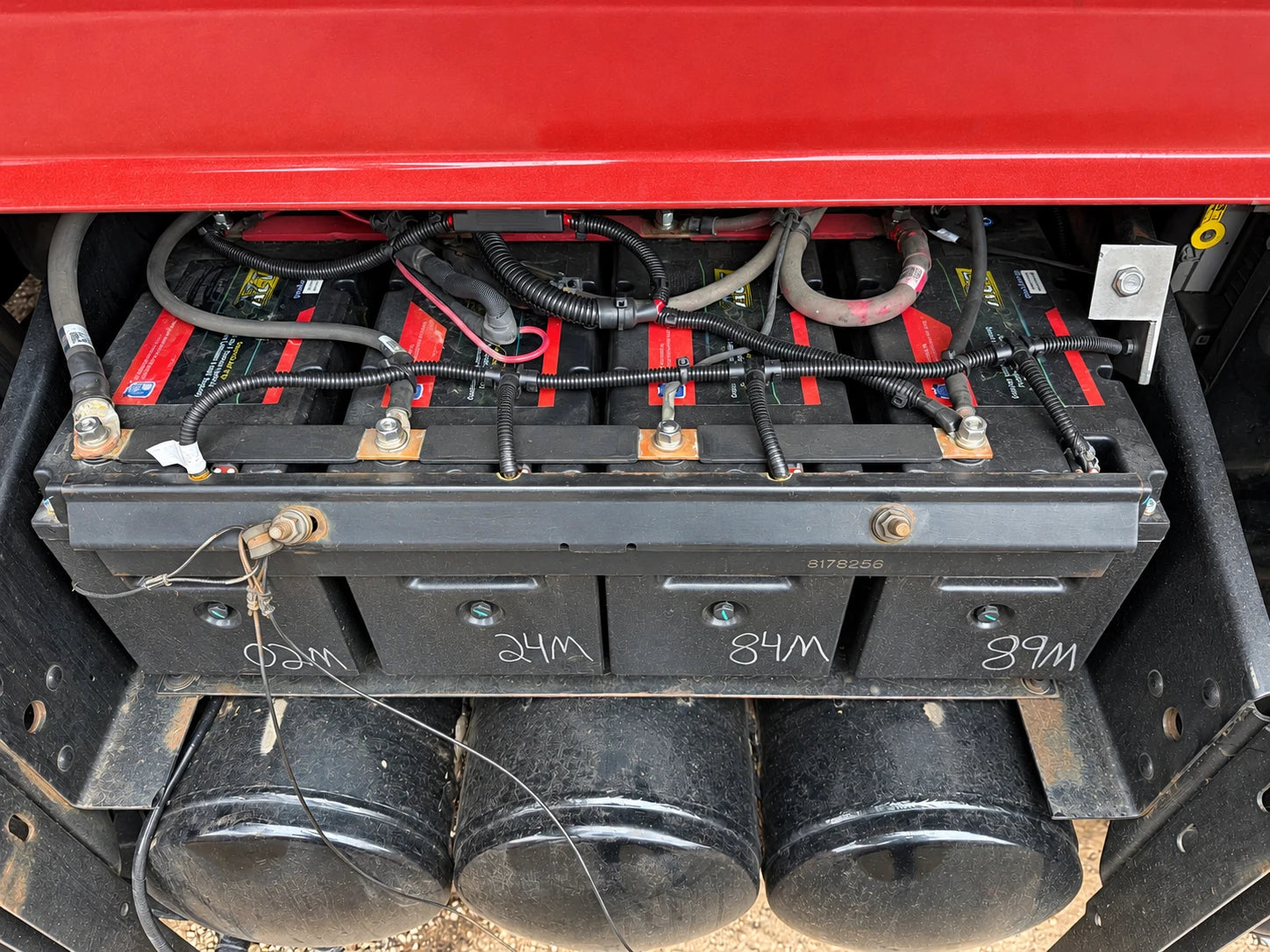 Battery bank beneath red truck bodywork with retaining rails and cable harness