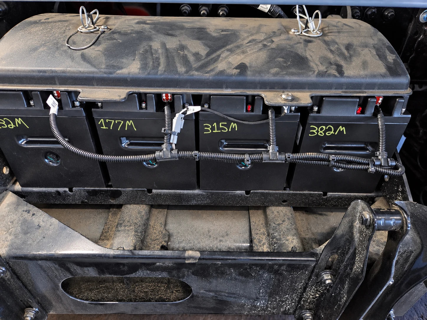Battery bank with communication harness beneath a protective top cover